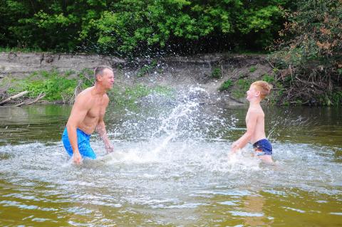 An adult and a child splashing each other with water in a river.