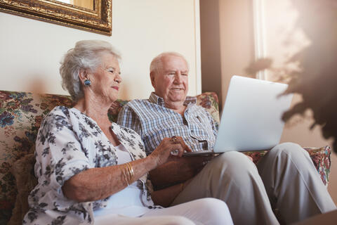Two adults sitting in a couch looking at a laptop.