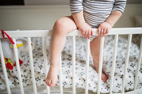 Toddler climbing out of crib, legs view.