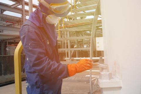 Worker wearing safety mask and protective clothing painting in manufacturing plant