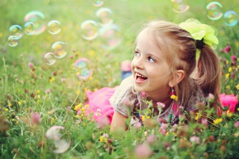 Young smiling child laying in the meadow looking at floating bubbles
