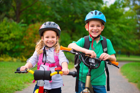 Two smiling children with their bicycles on a bike path.