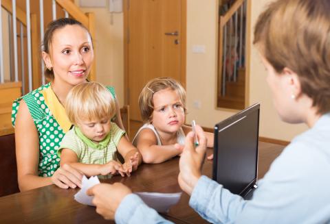 Two children sitting on a person's lap with another person discussing an issue
