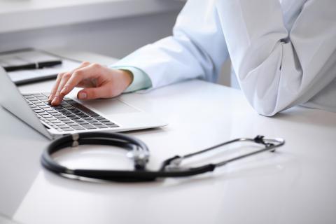Doctor's hand on a laptop next to a stethoscope
