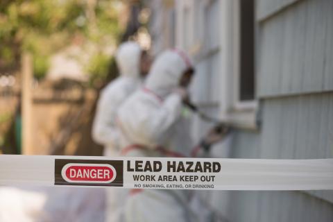 Danger, Lead Hazard tape and adults in hazmat suits removing lead paint outside