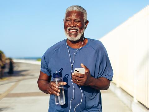 An older adult holds a water bottle and listens to music while running