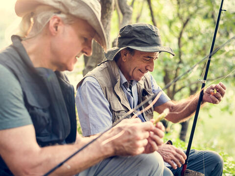 Two older adults tying lures to their fishing poles.