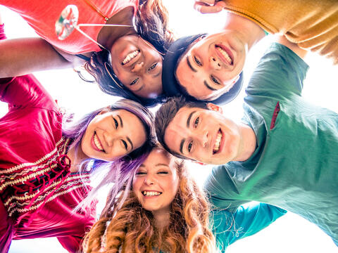 Faces of five teens with heads together looking down