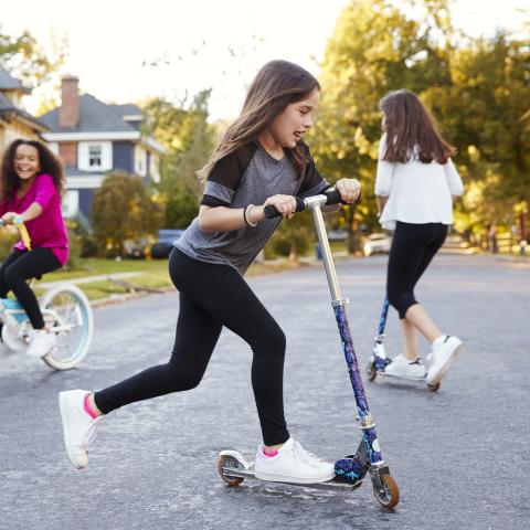 Three children riding bikes and scooters on the street.