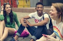 Three adults sitting on the ground talking and laughing.