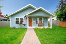 light blue house with white trim and porch with a flag on porch