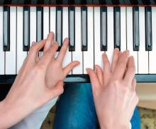 A pair of hands over child's hands on piano keys.
