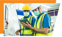 Two adults in safety vests and hardhats looking at a tablet