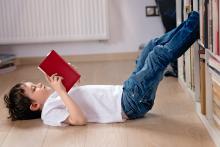 A child reads a book with his feet up on a bookcase