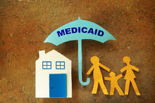 Paper cutouts house and people under Medicaid umbrella