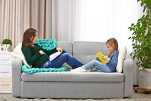 Pregnant mom and child sitting facing each other on a couch reading their books