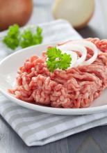 Raw ground beef with raw onion rings and garnish in a white plate on top of checkered napkin.