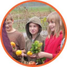 Circle image of school children holding vegetables at a farm.