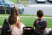 Two costumed children sit on steps next to bowl of candy waiting for trick or treaters