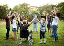 A group of adults and children raise joined hands while standing outside.