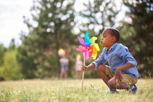 Kid blows into a giant pinwheel at the park