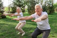 Two older adults doing squats while exercising in a park