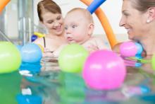 Two adults with a baby in a swimming pool.