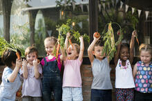 Seven smiling children hold vegetables from a garden
