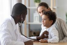 Child sitting on adult's lap while doctor listens to their heart