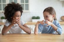Two children sitting at a counter drinking water and laughing