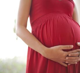 Clasped hands lay across her pregnant belly in red dress