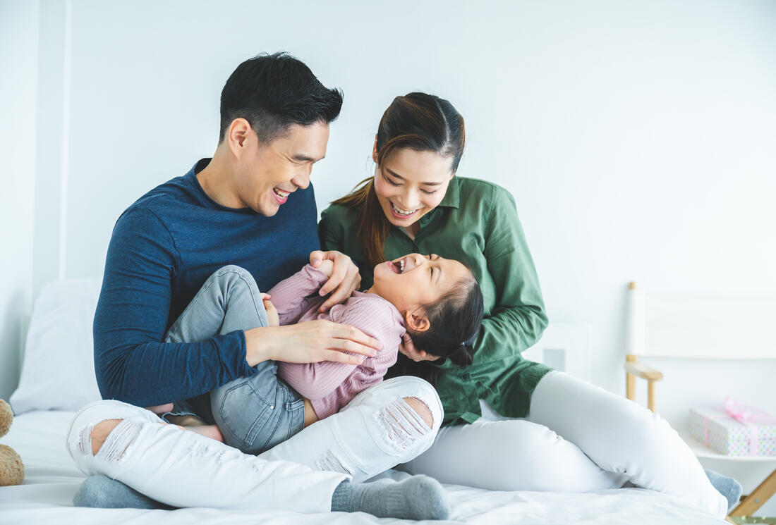 Two laughing adults and a child sitting on a bed